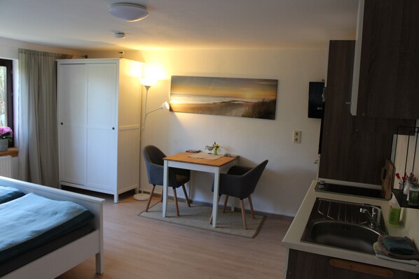 Une chambre d’hôtel comprenant un lit, un bureau avec deux chaises, un tableau au mur, une lampe et un coin cuisine avec un évier.