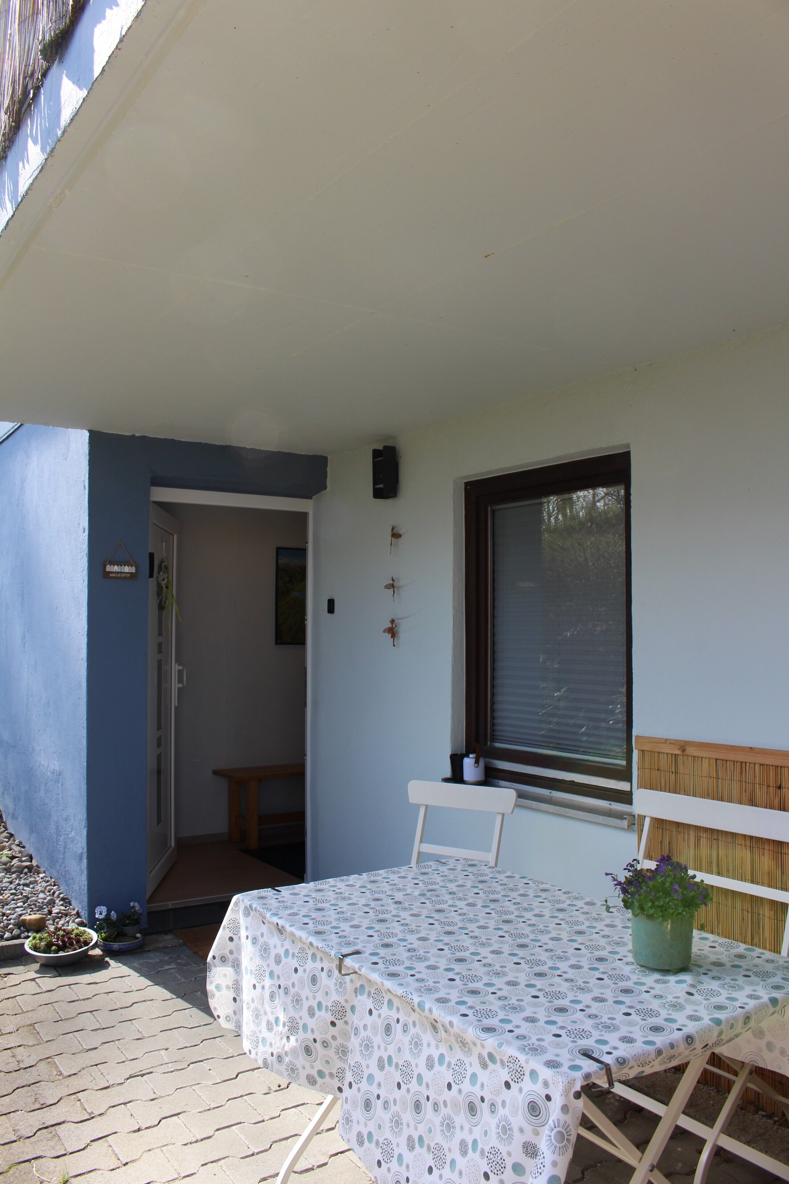 Un pequeño patio con una mesa y sillas, una planta en maceta y una ventana con persianas.