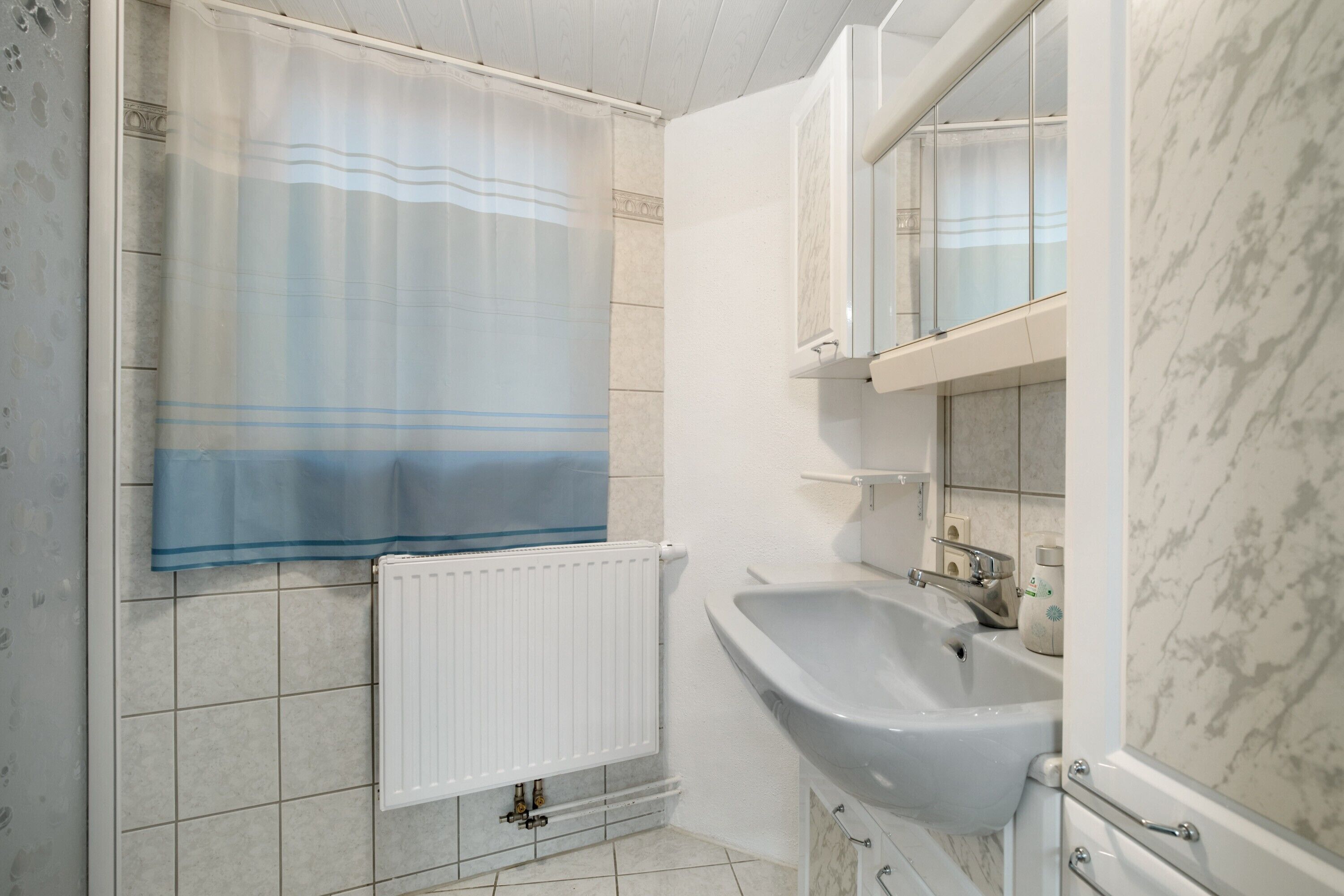 Une salle de bain équipée d’une douche, d’un lavabo, d’un miroir et d’un radiateur.