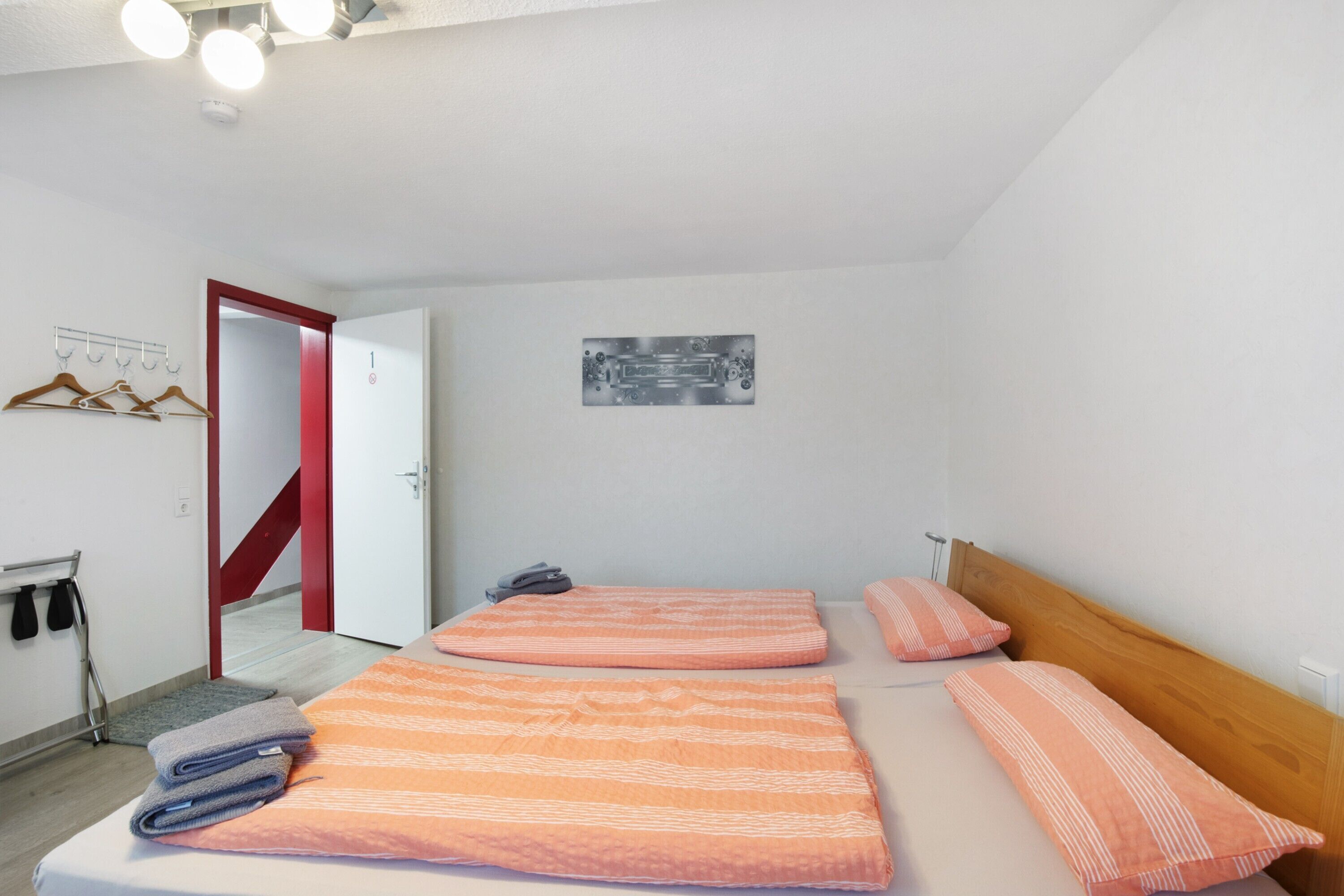 Un dormitorio con dos camas, una puerta roja, un perchero y un pequeño cuadro en la pared.