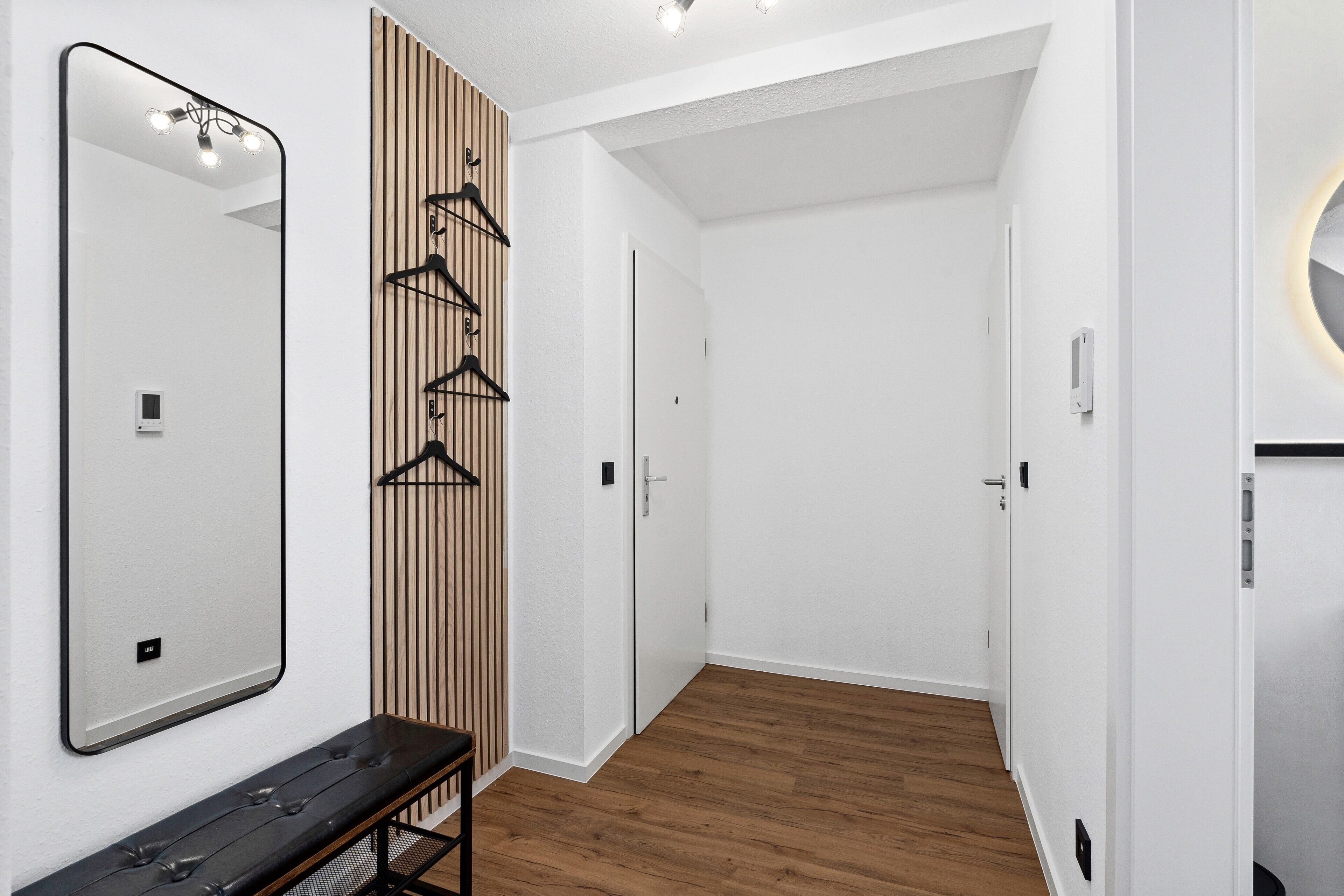 A hallway with a mirror, wooden panel, bench, and a door.