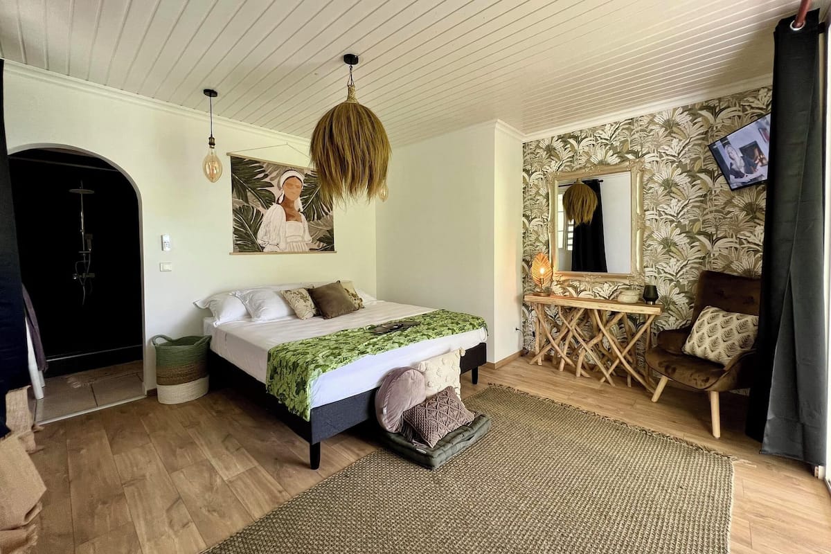 A bedroom with a bed, a hanging light fixture, a mirror, a small table, and a chair.
