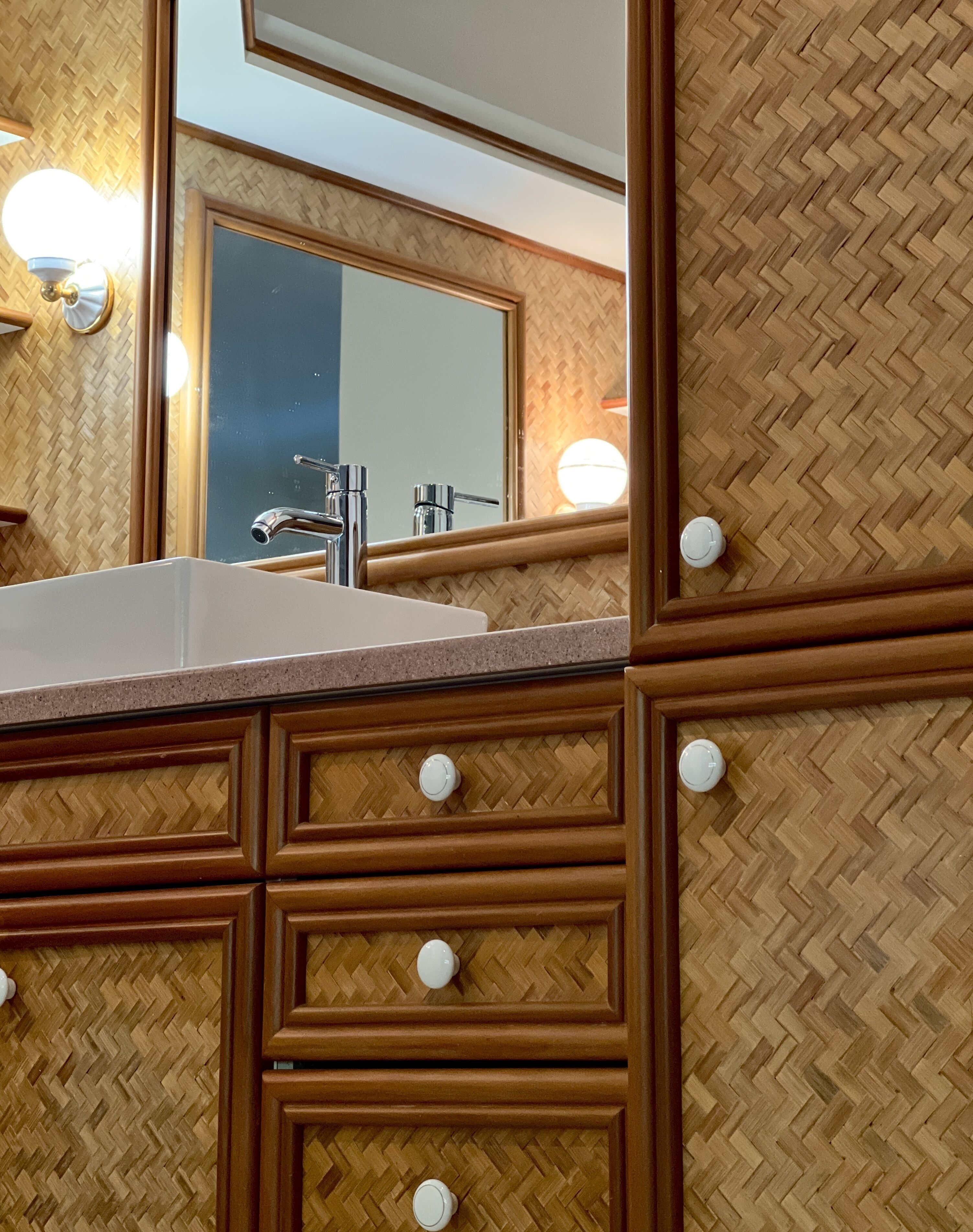Un baño con pared de madera en patrón espiga, un lavabo blanco y un espejo con iluminación.