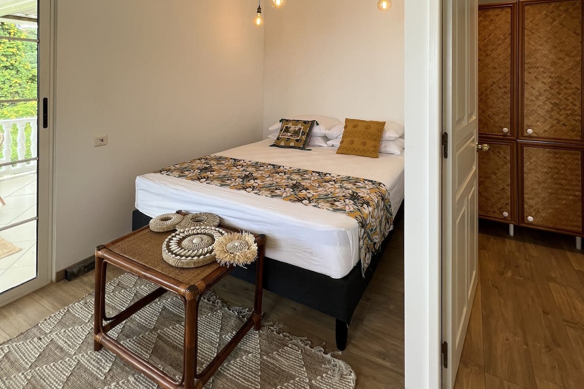 A bedroom with a bed, a small table, a patterned rug, and a wooden wardrobe.