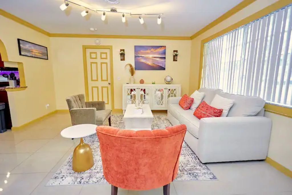 A living room with a white sofa, a pink chair, a coffee table, and a TV.