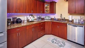 A modern kitchen with wooden cabinets, granite countertops, a built-in microwave, and a dishwasher. - The Royal Oasis heated pool (Lake Worth)