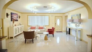 A spacious living room with a white sofa, a red armchair, a coffee table, and a white console table with a mirror. - The Royal Oasis heated pool (Lake Worth)