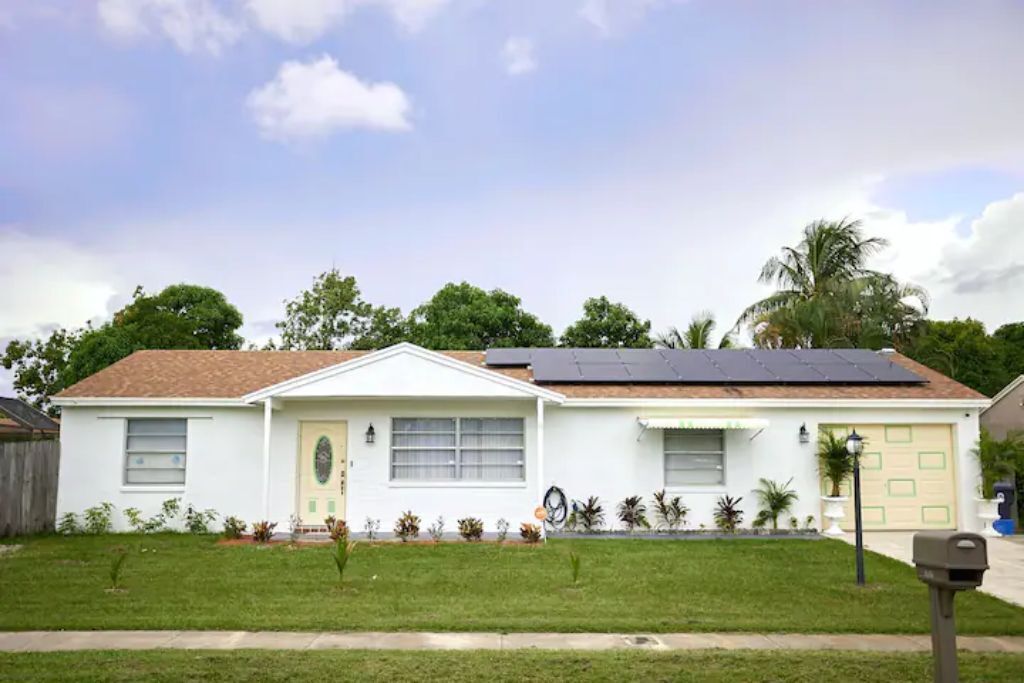 Une maison de plain-pied avec un panneau solaire sur le toit, une petite cour avant agrémentée de quelques plantes et une boîte aux lettres.