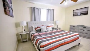 A bedroom with a bed, nightstands, a dresser, and a ceiling fan. - The Royal Oasis heated pool (Lake Worth)