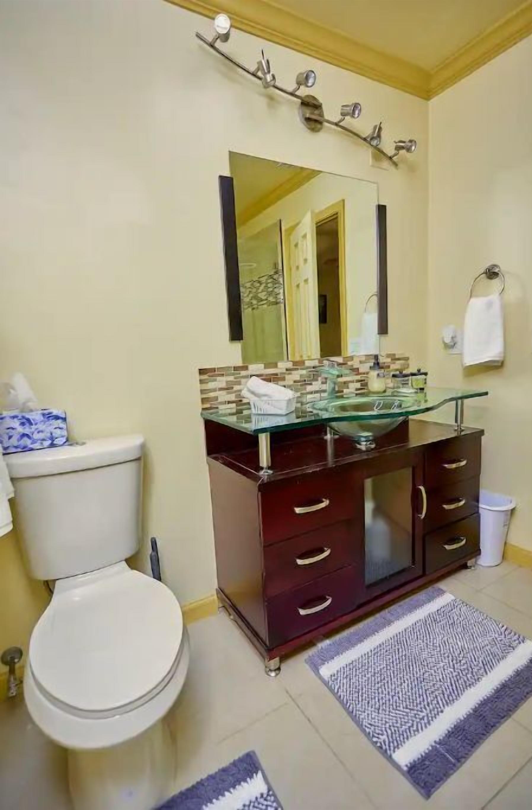 Ein Badezimmer mit einem Glasbecken, einem dunklen Holzschrank, einer weißen Toilette und einem Spiegel über dem Becken.