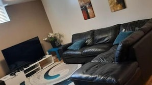 A living room with a black leather sofa, a flat-screen TV, and a decorative rug.