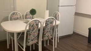 A small dining area with a white table and chairs, a small potted plant, and a white refrigerator.