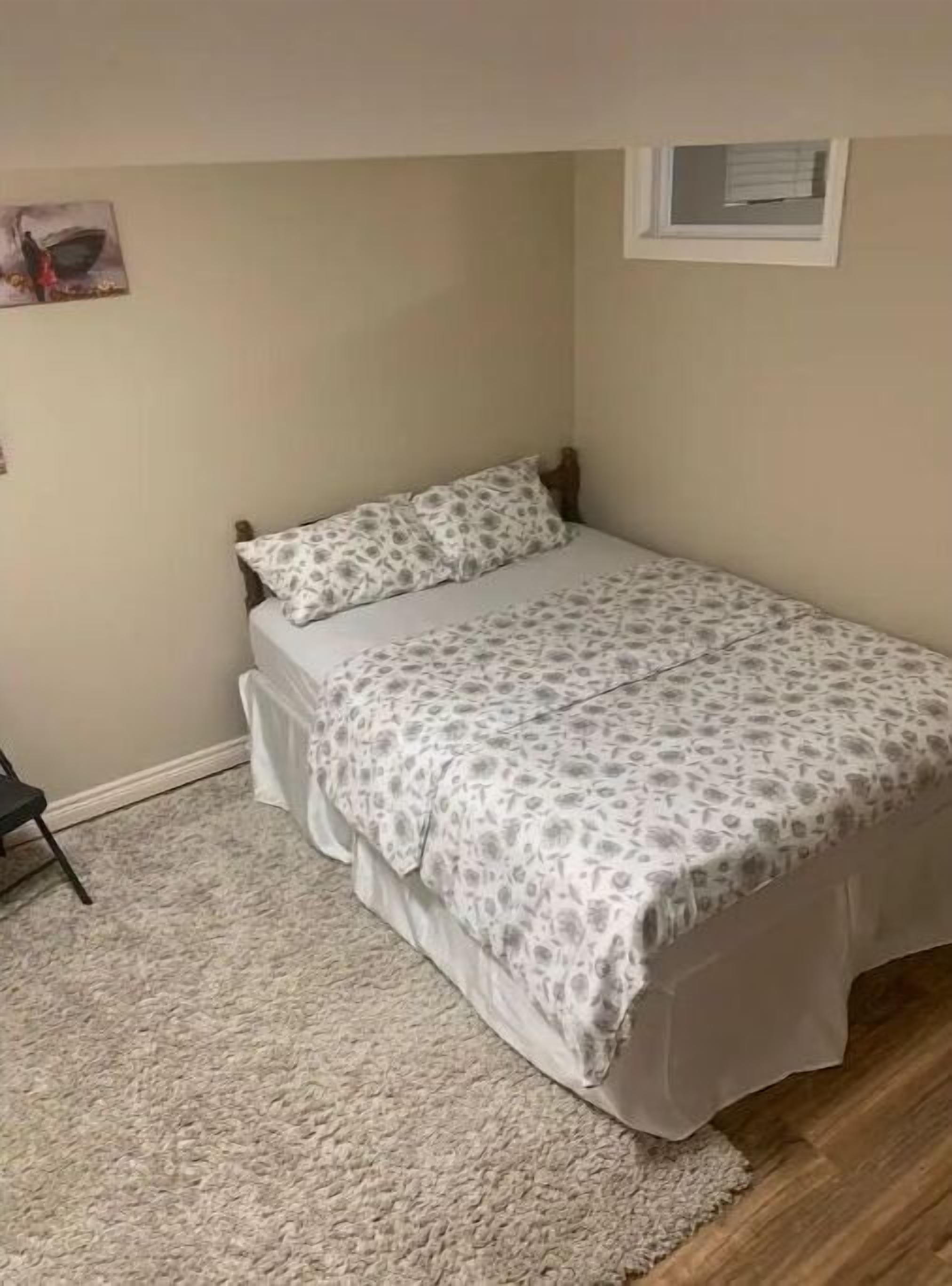 A small bedroom with a single bed, a window, and a carpeted floor.