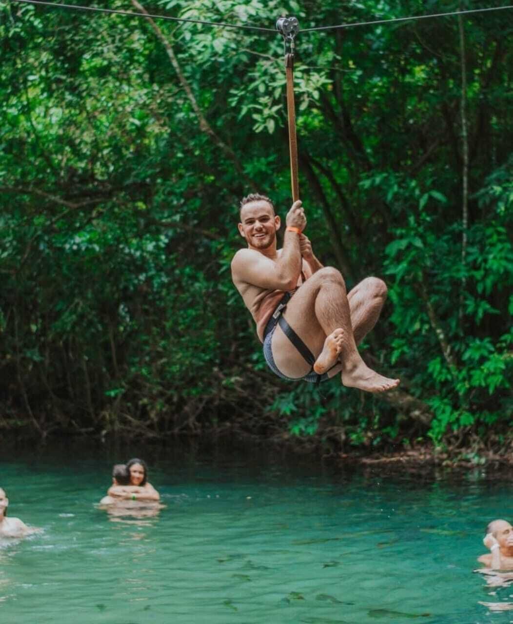 A person suspended by a rope in a natural setting with water and greenery.