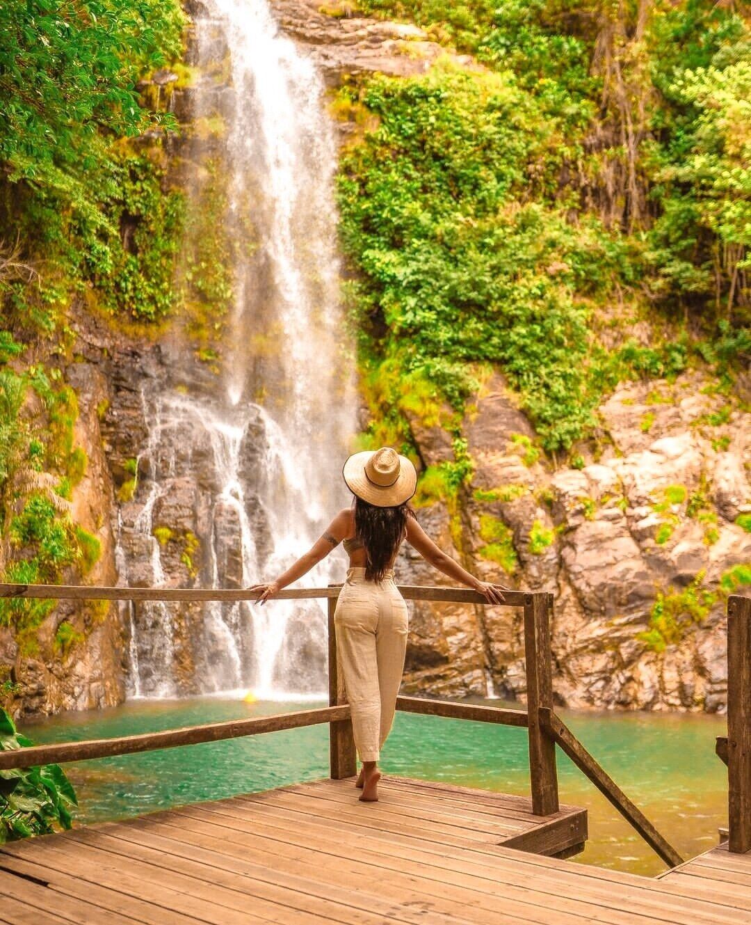 A wooden deck with a railing overlooking a waterfall and a turquoise pool.