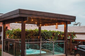 A covered outdoor area with a glass balustrade, a hot tub, and string lights. - Lukinhas Pousada  (Nobres)