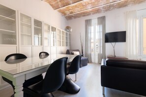 Un salon moderne avec une table à manger en verre, des chaises noires, un canapé, un téléviseur à écran plat et une grande fenêtre avec des rideaux.