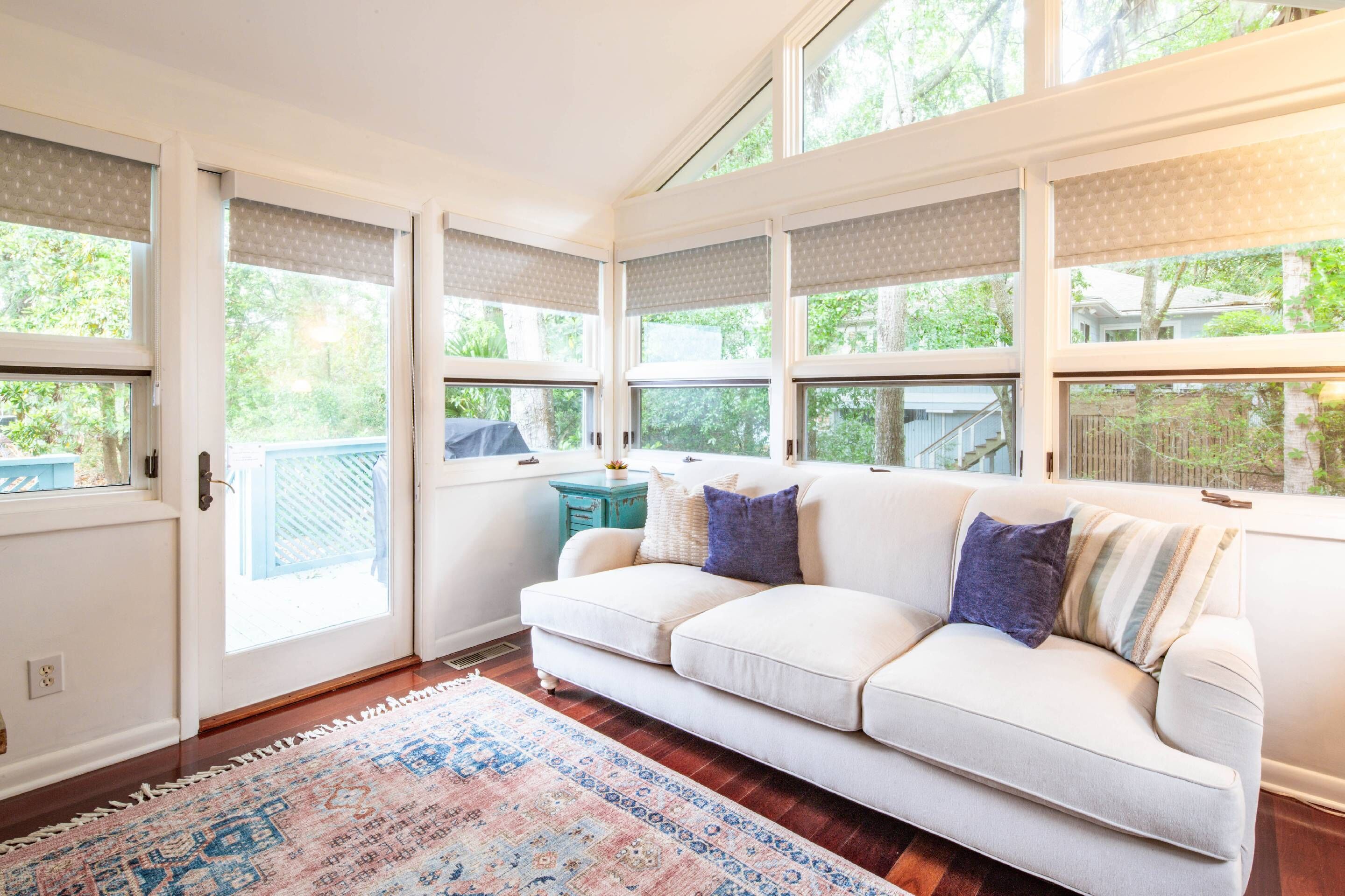 A room with a white sofa, a patterned rug, and a view of greenery outside.