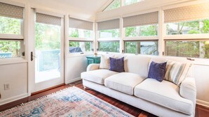 Une pièce avec un canapé blanc, un tapis à motifs et une vue sur la verdure à l’extérieur.