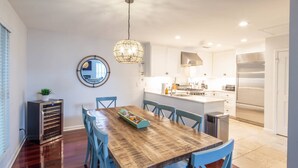 Une cuisine moderne avec des meubles blancs, des appareils en acier inoxydable et une table à manger en bois, assortie de chaises bleues.