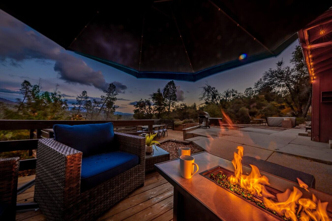 Eine Terrasse im Freien mit Feuerstelle, Sitzgelegenheiten und Blick auf die Landschaft.