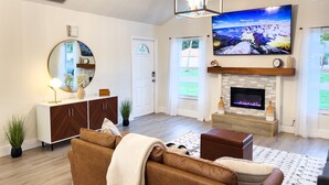 A modern living room with a large flat-screen TV, a fireplace, a sofa, and a decorative mirror. - Coastal Gem: Pool, Hot Tub, King Bed, & More (Port St. Lucie)