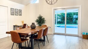 A dining area with a wooden table, brown chairs, a vase, and a large clock on the wall. - Coastal Gem: Pool, Hot Tub, King Bed, & More (Port St. Lucie)