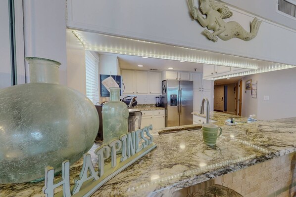 A modern kitchen with marble countertops, stainless steel appliances, and a decorative mermaid sculpture.