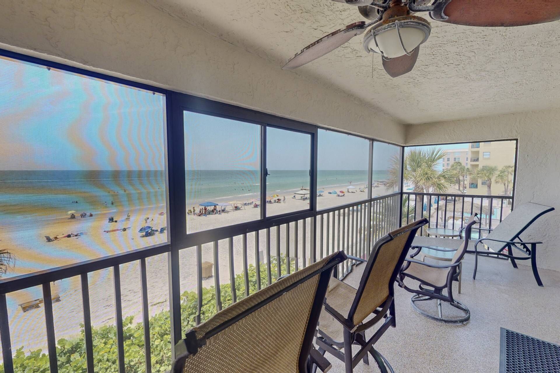 Een balkon met uitzicht op het strand en de oceaan. Er staan stoelen en een tafel op het balkon.