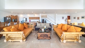 A spacious living area with two bamboo sofas, a central coffee table, and a kitchen in the background. - Villa Dahlia Manggis - 4 bed Oceanfront Retreat, with Chef & Butler Candidasa (Manggis, Karangasem)