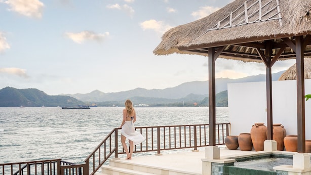 A woman standing on a deck overlooking a pool with a view of the sea and mountains. - Villa Dahlia Manggis - 4 bed Oceanfront Retreat, with Chef & Butler Candidasa (Manggis, Karangasem)