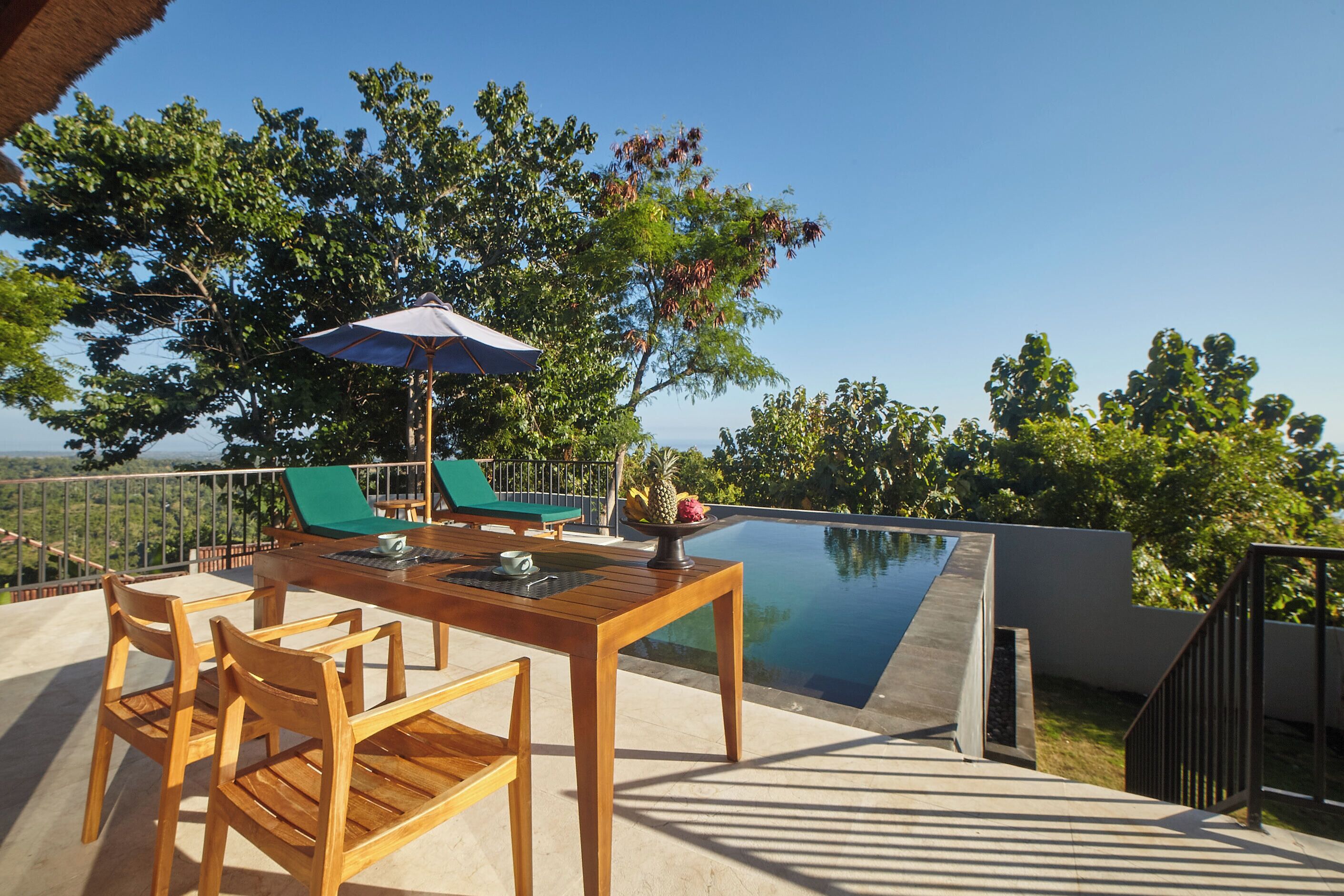 A wooden deck with a pool, green lounge chairs, and a table with chairs.
