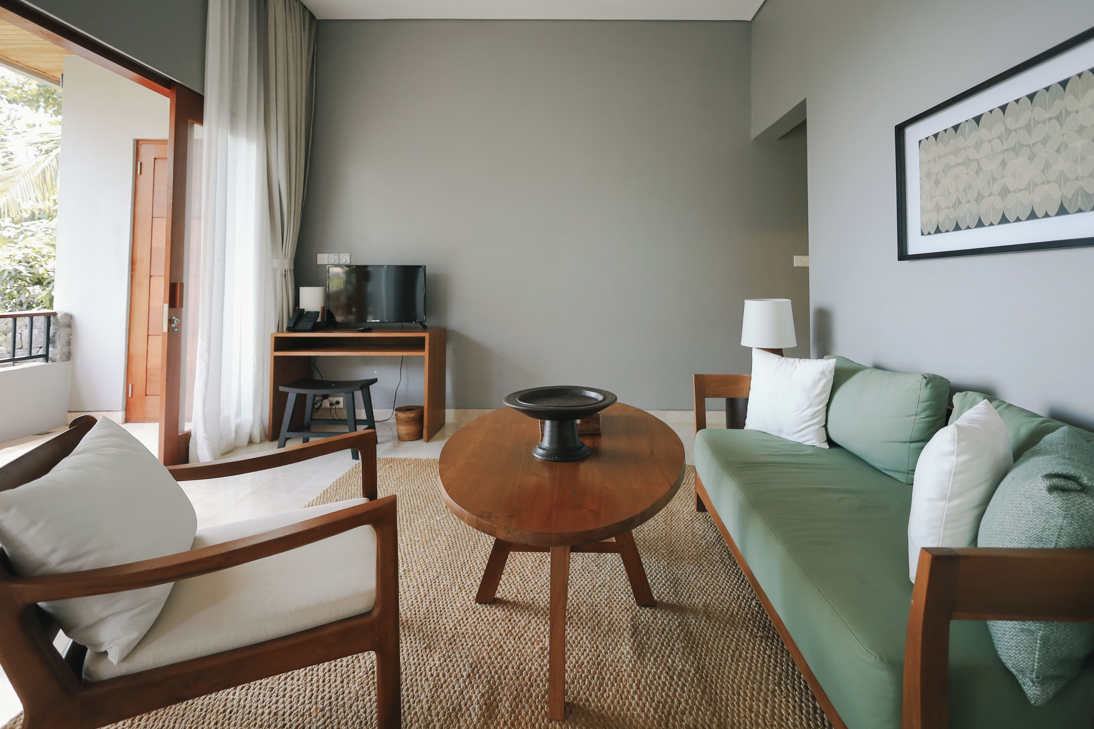 A room with a green sofa, wooden chairs, a round wooden table, a television on a stand, and a framed picture on the wall.