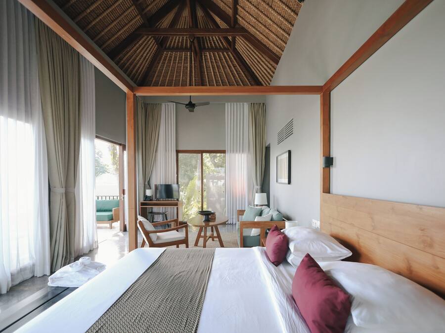 A hotel room with a large bed, a wooden headboard, a desk with a chair, a television, and a balcony with curtains.