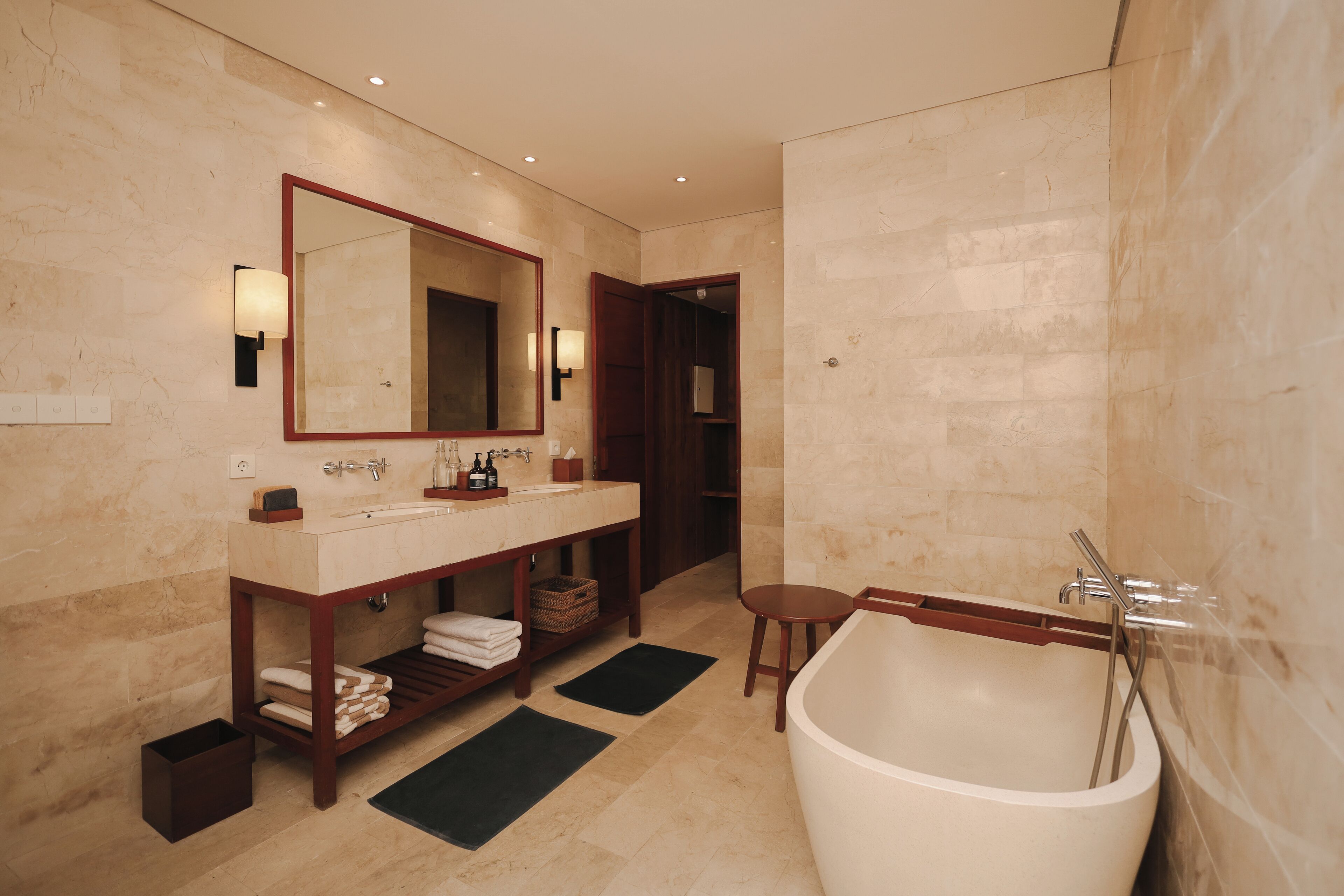 Un baño moderno con una bañera grande, dos lavamanos, un espejo y un mueble de tocador de madera.