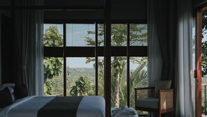 A bedroom with a large window, a bed, a chair, and a small table with towels. - Sanglung Villas (Kubutambahan)