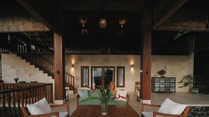 A spacious indoor area with a wooden table, two chairs, a sofa, and a staircase. - Sanglung Villas (Kubutambahan)
