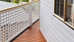 Une véranda couverte avec un plancher en bois, des balustrades blanches et une grande fenêtre munie d’un moustiquaire.