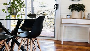 Un espace repas avec une table en verre, des chaises noires et un mur en pierre à l’extérieur.