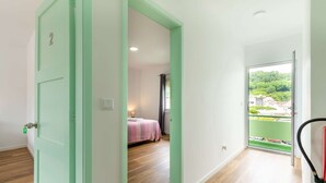 A room with a bed, a window with a view of greenery, and a door with a number.