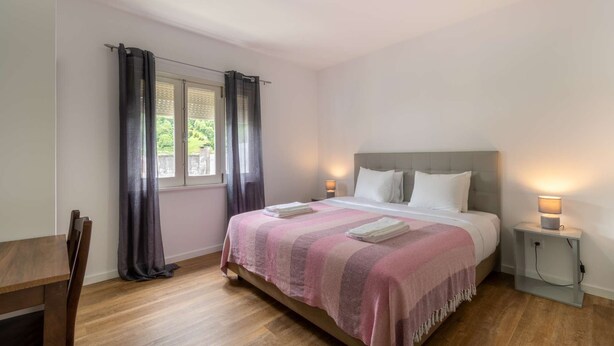 A bedroom with a bed, bedside tables, a desk, and a window with curtains.