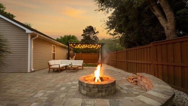 A backyard with a stone fire pit, outdoor furniture, and a wooden fence. - Beach Time! w/ King Beds, Pool, Fire Pit, & Tennis (Wilmington)