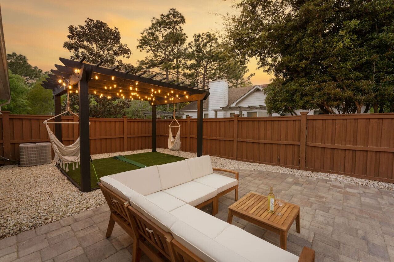 An outdoor patio with a wooden pergola, white cushioned seating, and a small table.