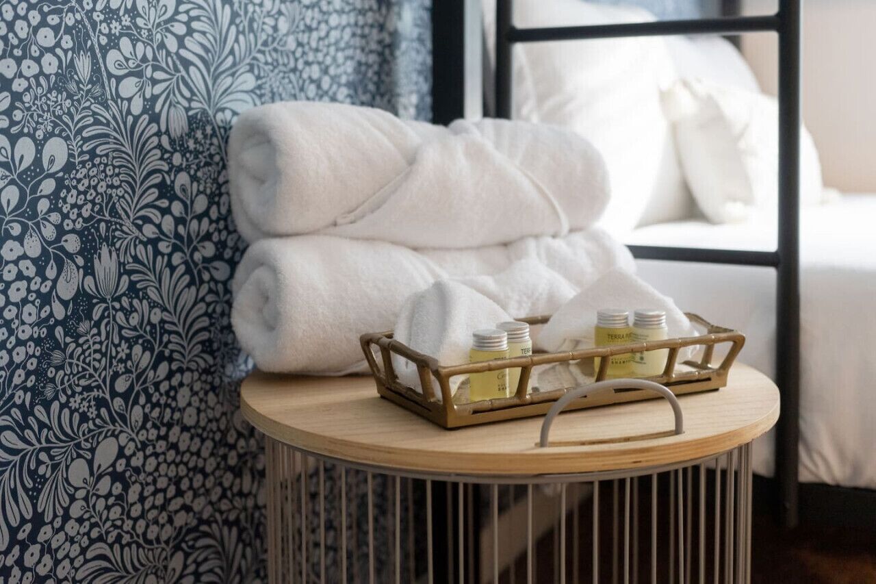 A neatly folded white towel stacked on a round wooden table, with a tray containing two bottles of lotion and a small container.