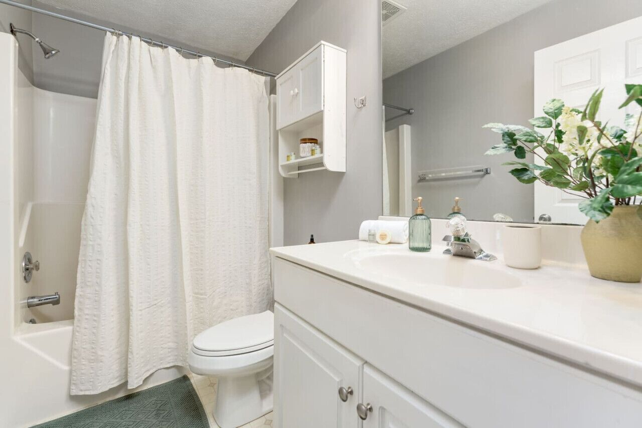 Et badeværelse med badekar, toilet, hvid kommode og en potteplante.