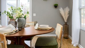 A dining area with a round table set for four, surrounded by chairs. There are potted plants on the wall and a vase with white feathers. - Beach Time! w/ King Beds, Pool, Fire Pit, & Tennis (Wilmington)