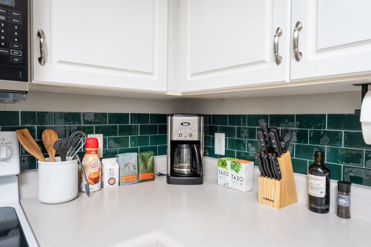 A kitchen with white cabinets, a coffee maker, a knife block, and various coffee products on the counter.