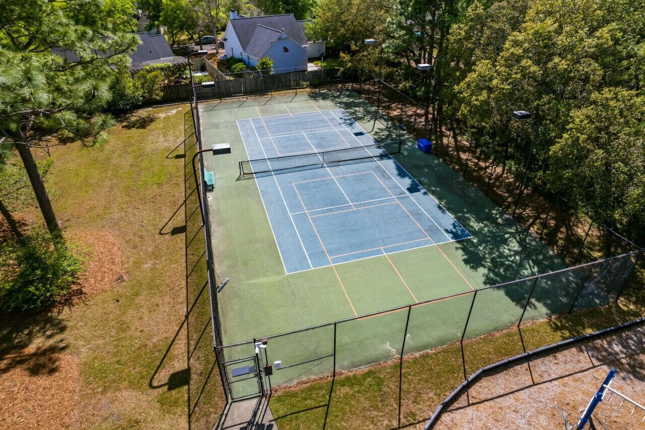 Un court de tennis en plein air, entouré d’arbres et bordé d’une maison.