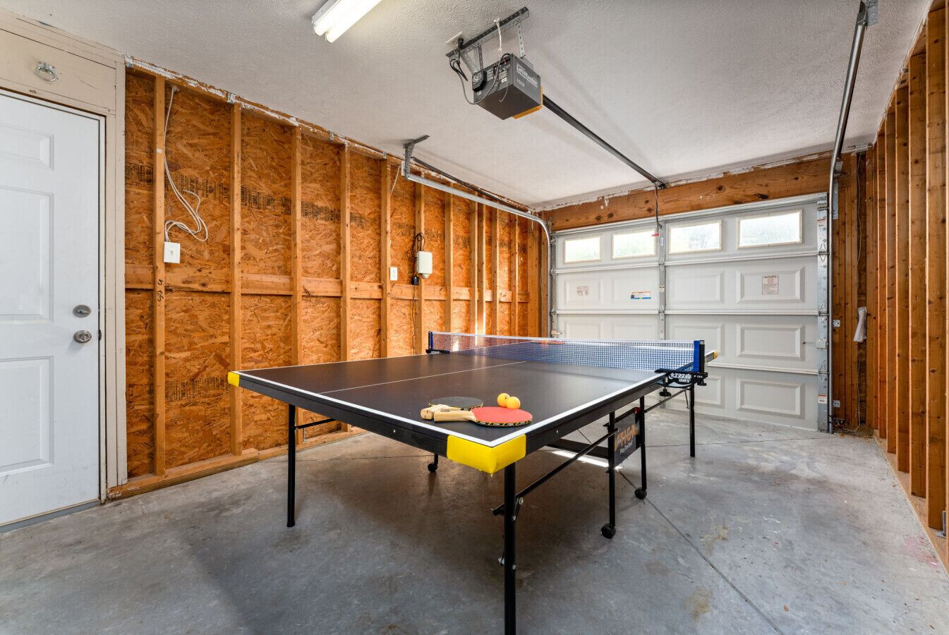 Ein Pingpongtisch in einer Garage mit Holzwänden und einer weißen Tür.