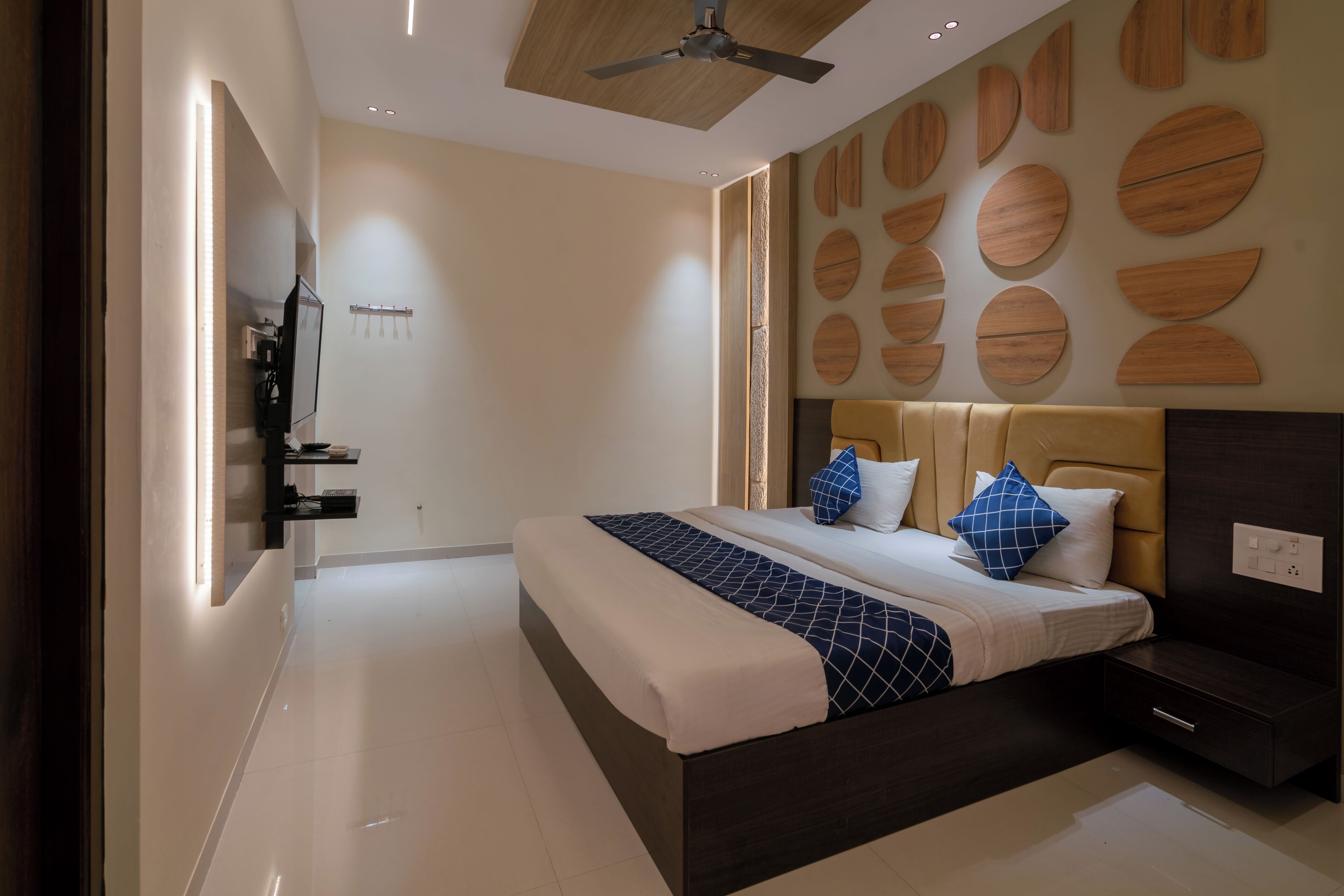 A modern bedroom with a large bed, a ceiling fan, and a wall with circular wooden panels.